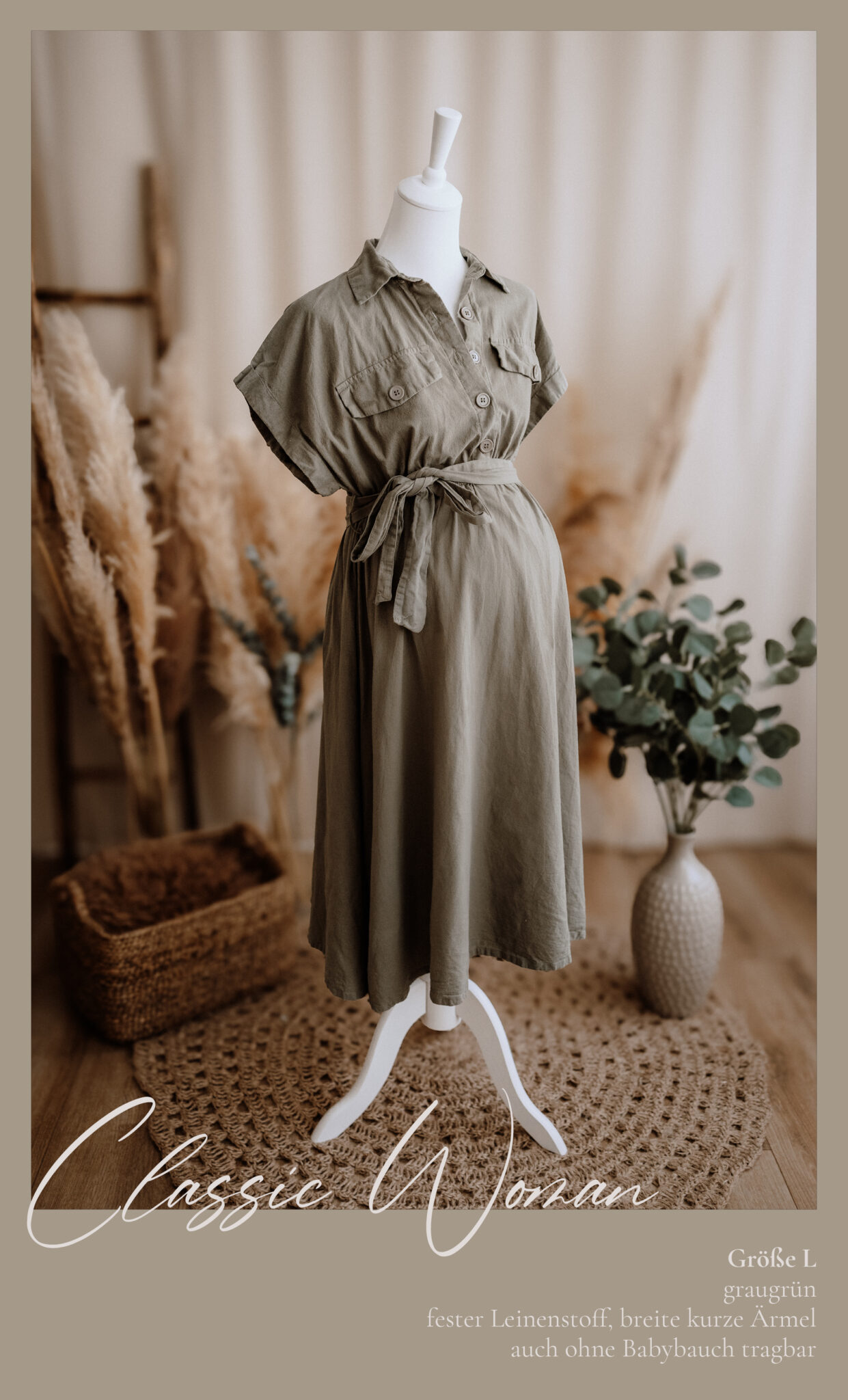 Ein khakigrünes, geknöpftes Kleid mit kurzen Ärmeln und einem Gürtel in der Taille ist auf einer Schaufensterpuppe ausgestellt. Die Einrichtung umfasst natürliche Dekorelemente wie Körbe, Pampasgras und grünes Laub auf einem gewebten Teppich.