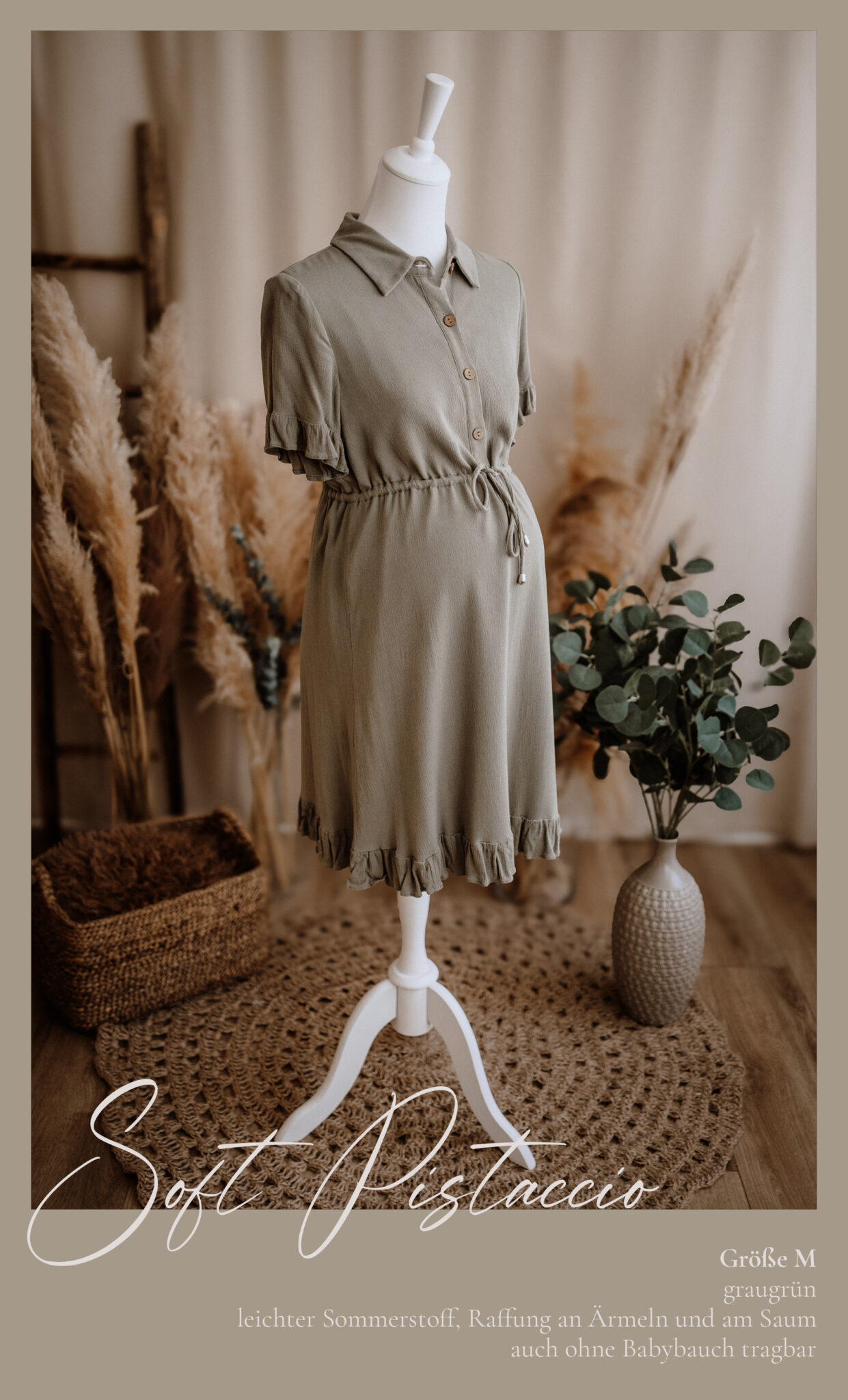 Ein salbeigrünes Umstandskleid mit kurzen Ärmeln, enger Taille und Rüschendetails wird auf einer Schaufensterpuppe präsentiert. Die Szene zeigt Pampasgras, einen geflochtenen Korb und einen strukturierten Teppich, der eine weiche, natürliche Ästhetik hervorruft.