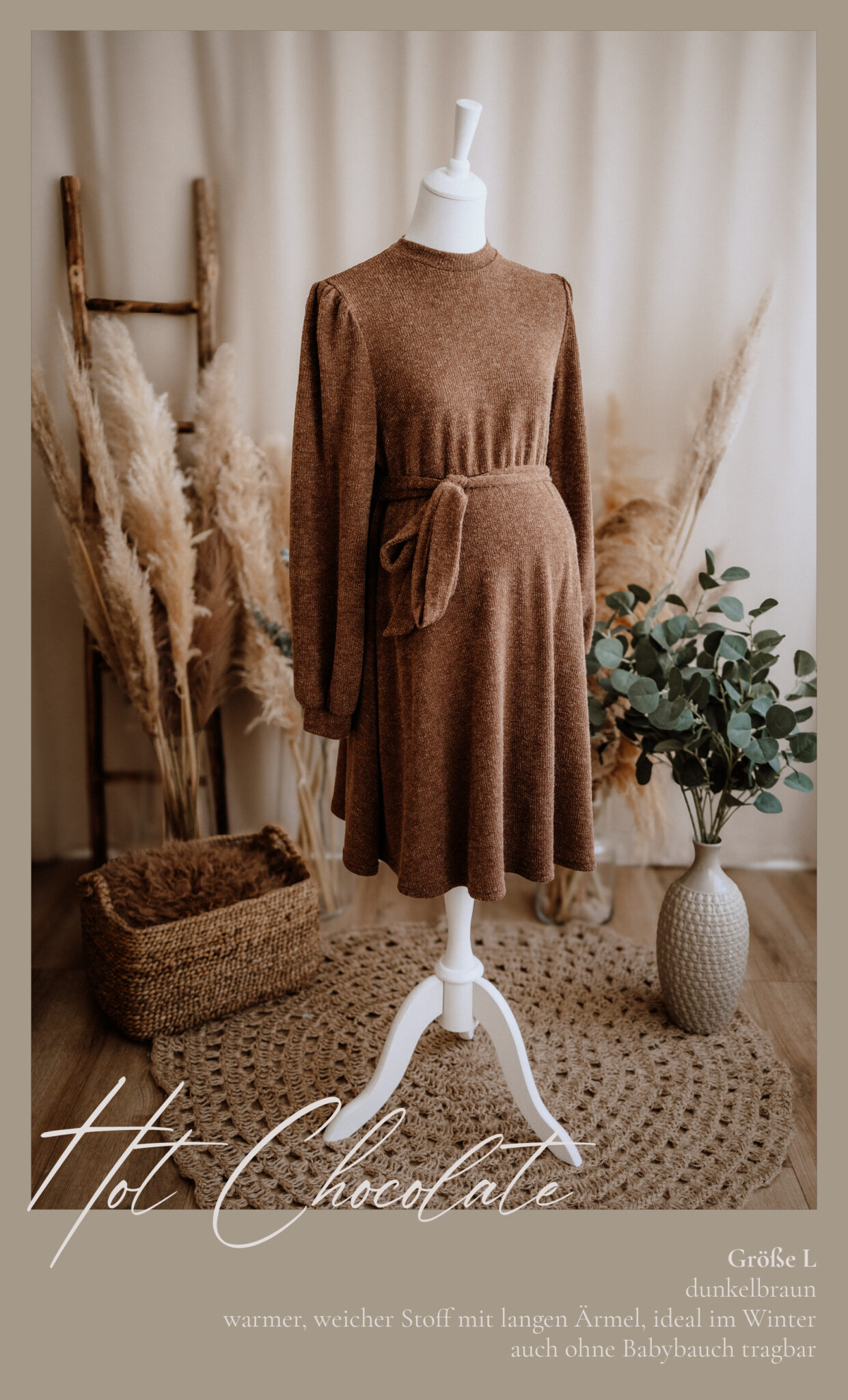Ein braunes, langärmeliges Umstandskleid mit Taillenband ist auf einer weißen Schaufensterpuppe ausgestellt. Die Szene enthält Pampasgras, einen geflochtenen Korb, einen runden Teppich und eine dekorative Vase, alles in warmen, neutralen Tönen.